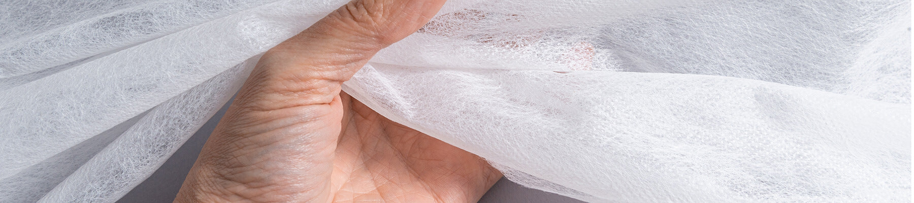 A person's left hand holding non-woven, disposable linens