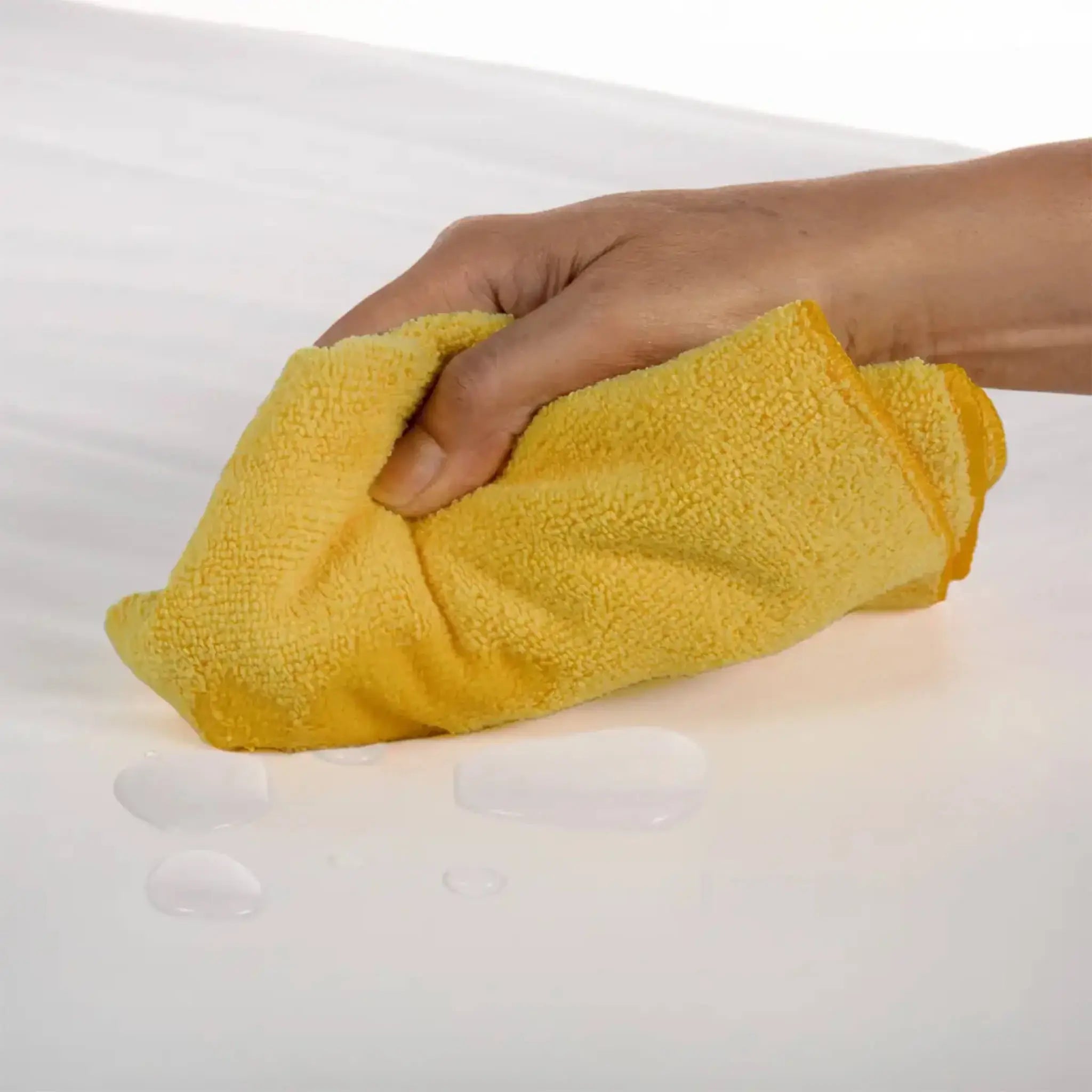 Person cleaning a white surface with a yellow microfiber cloth