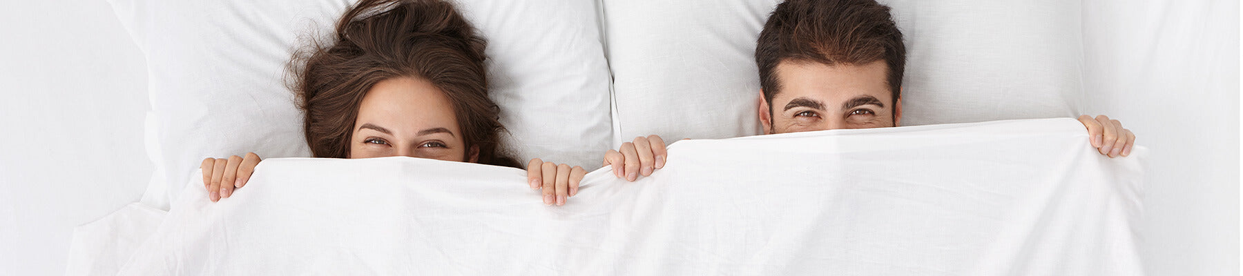 man and woman peeking out of bed sheets